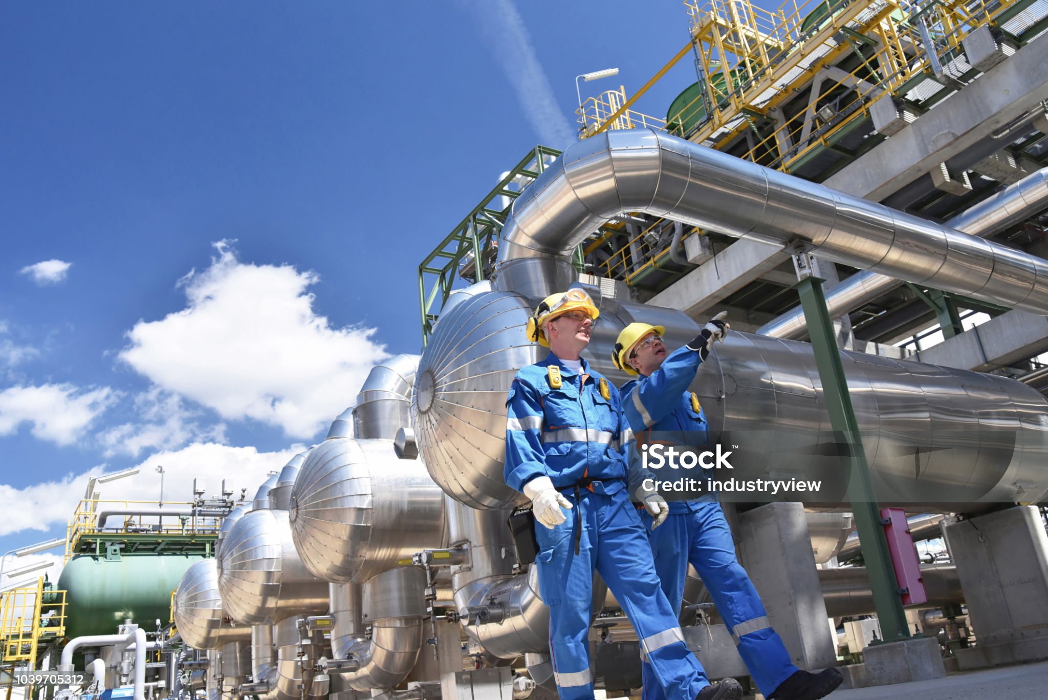 Two engineers in safety gear inspecting large industrial pipes outdoors.