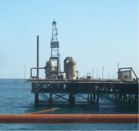 A rusty, abandoned offshore drilling rig stands on stilts in the sea.